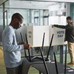 Homens preparam cabines de votação em um ambiente interno para o dia da eleição.