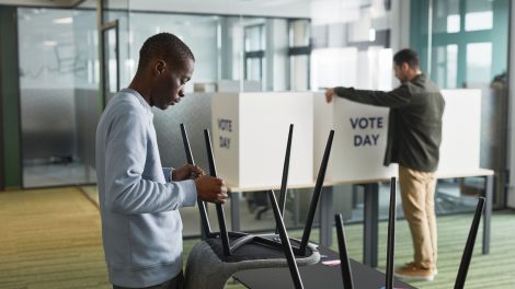 Homens preparam cabines de votação em um ambiente interno para o dia da eleição.