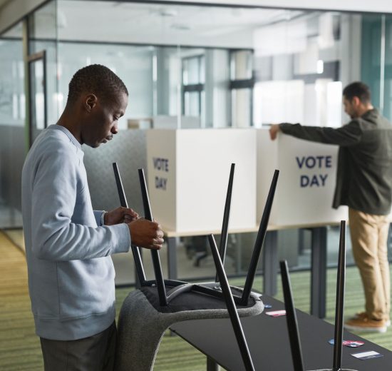 Homens preparam cabines de votação em um ambiente interno para o dia da eleição.