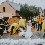 Equipe de emergência enche sacos de areia em uma rua sob chuva para ajudar a conter alagamentos.