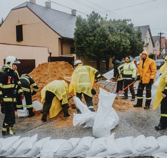 Equipe de emergência enche sacos de areia em uma rua sob chuva para ajudar a conter alagamentos.