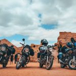 Grupo de motocicletas estacionadas com seus condutores diante de uma paisagem rochosa.