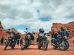 Grupo de motocicletas estacionadas com seus condutores diante de uma paisagem rochosa.
