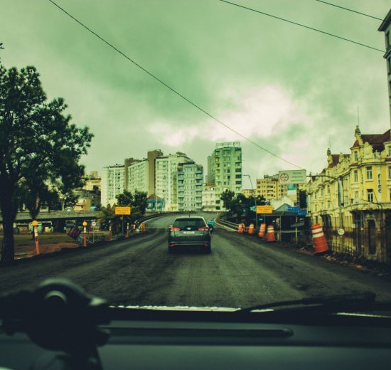 Obras viárias em andamento em uma rua cercada por prédios e estruturas urbanas.