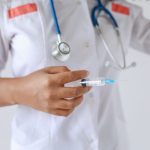 Profissional de saúde de jaleco branco segura uma seringa preparada para aplicação.