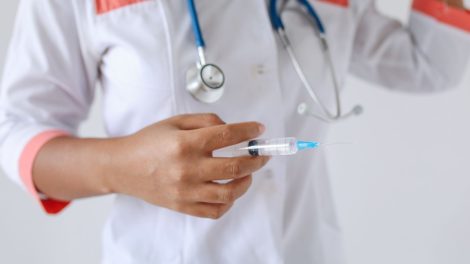 Profissional de saúde de jaleco branco segura uma seringa preparada para aplicação.