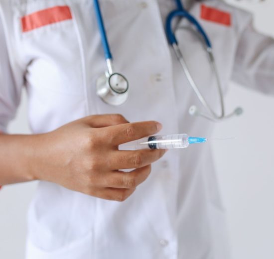 Profissional de saúde de jaleco branco segura uma seringa preparada para aplicação.