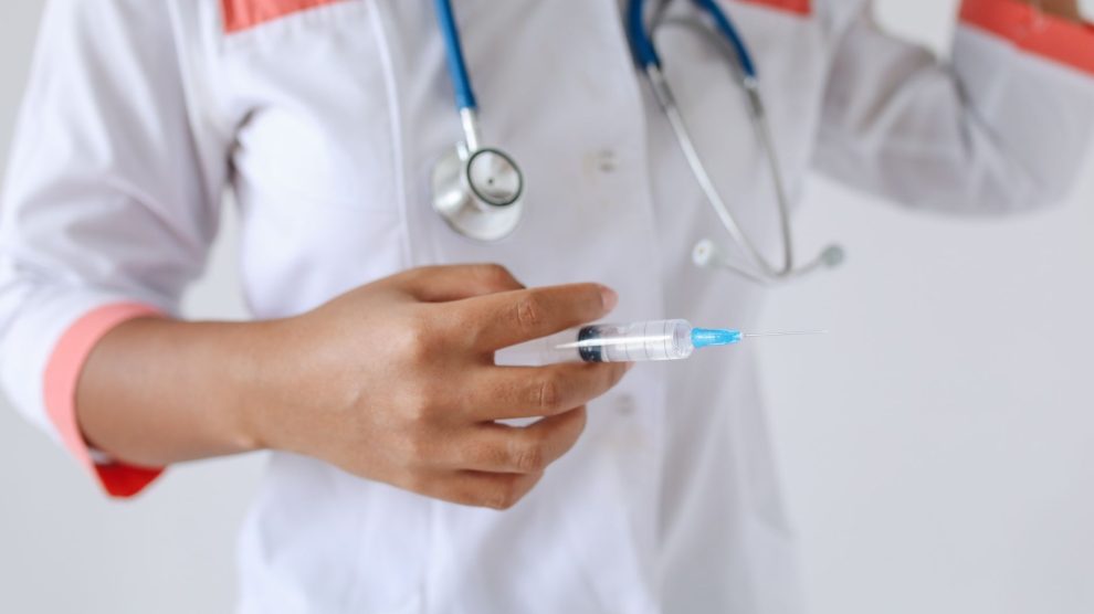 Profissional de saúde de jaleco branco segura uma seringa preparada para aplicação.