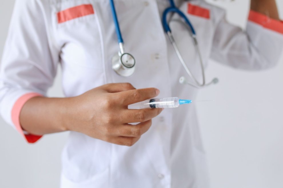 Profissional de saúde de jaleco branco segura uma seringa preparada para aplicação.